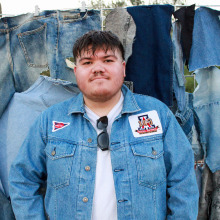 Young male college student posing in front of a denim backrop